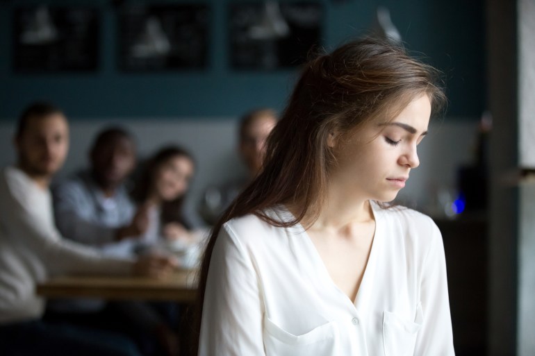 Sad young woman avoiding ignoring bad friends suffering from gossiping, bullying, unfair attitude or discrimination, frustrated millennial girl feeling upset, hurt and offended sitting alone in cafe