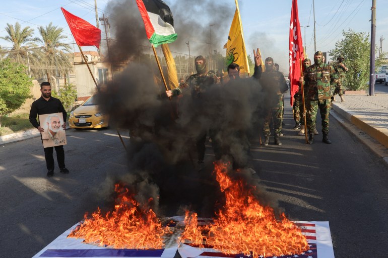 U.S. and Israeli national flags burn, as members of Harakat Hezbollah al Nujaba, gather next to fire during a protest in solidarity with Palestinians in Gaza, in Baghdad, Iraq, October 8, 2023. REUTERS/Ahmed Saad