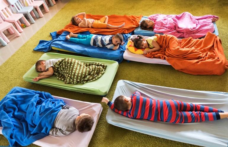 High angle view of group of tired kids in pajamas resting on beds at kindergarten.