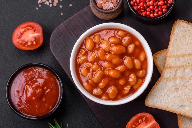 Delicious canned beans in a tomato in a white ceramic bowl on a dark concrete background