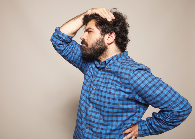 blue chequered shirt, hairy big man, feminine pose, hand on hip, hand on head, black curly hair, beard, beige background, studio lit, fashion