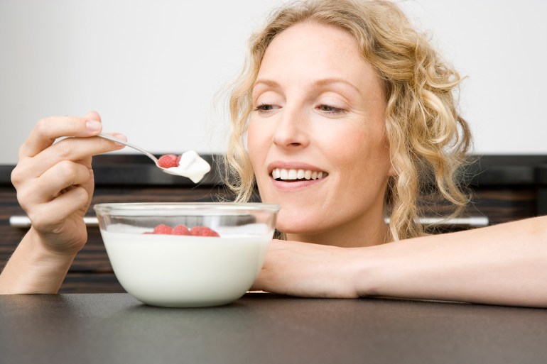 Smiling woman eating yogurt on sofa at home