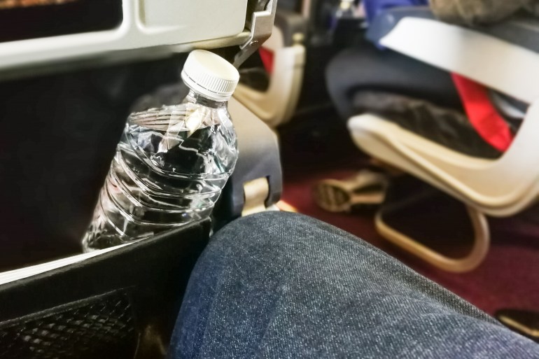 Passenger holding mineral water bottle in aeroplane cabin. Advice to drink lots of water to keep oneself hydrated on long haul flight.