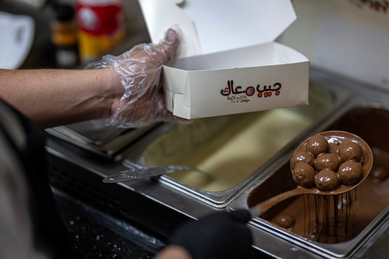 An employee submerges sweets in milk chocolate with traditional Sudanese taste at a restaurant run by a businessman who relocated to Cairo after fleeing the ongoing war in Sudan, on May 27, 2024. - Across the sprawling megalopolis of Cairo, home to 20 million people, many Sudanese refugees have opened businesses, bringing a taste of home and hoping to make a name for themselves. (Photo by Khaled DESOUKI / AFP)