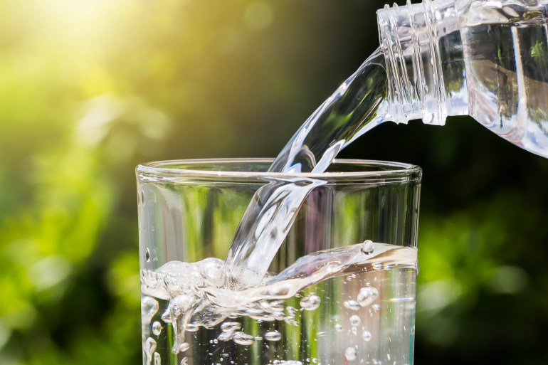 Drinking water pouring from bottle into glass on blurred green nature background