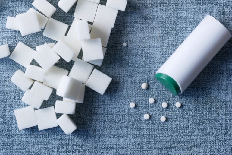 artificial sweetener and raw white sugar cube on table