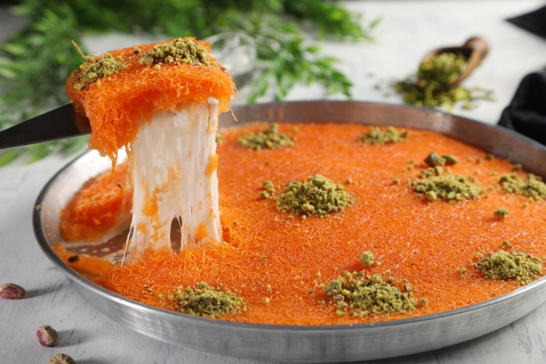 Arabic traditional kunafa. desserts rough konafa in tray sweet with pistachio and pine on top. close up