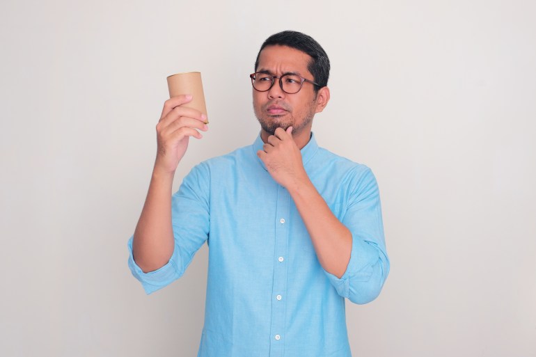 Adult Asian man looking to canned product that he hold with confuse expression