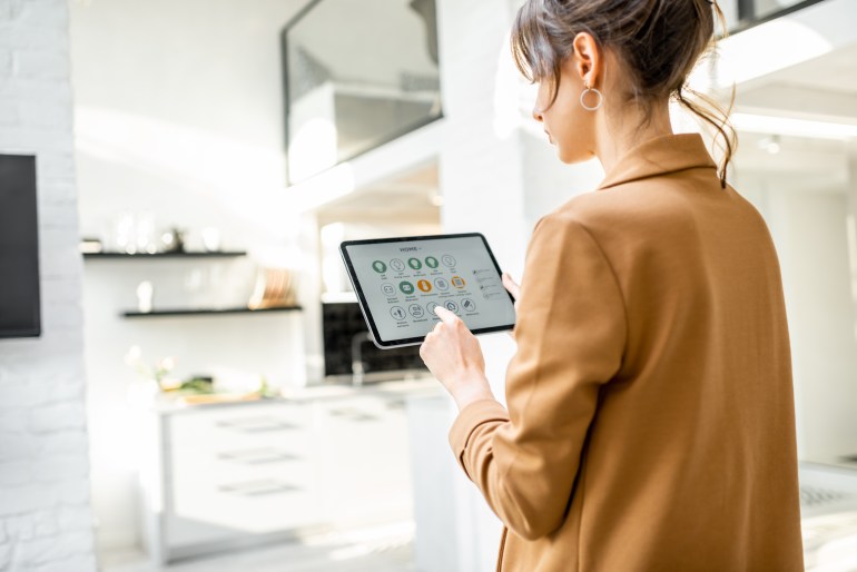 Woman controlling smart home devices using a digital tablet with launched application in the white living room. ...