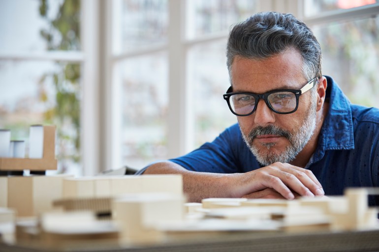 Mature male architect looking at building model in office