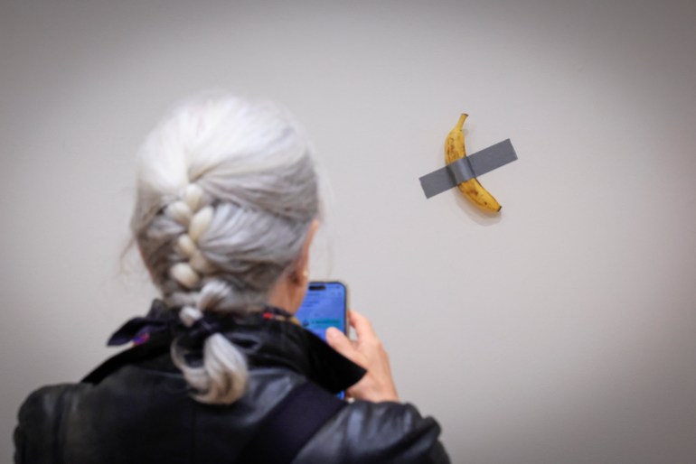 (FILES) A journalist takes a picture of Italian visual artist Maurizio Cattelan's duct-taped Banana entitled "Comedian," displayed during a media preview at Sotheby's in New York, on November 8, 2024. - A fresh banana taped to a wall -- a provocative work of conceptual art by Italian artist Maurizio Cattelan -- was bought for $6.2 million on November 20, 2024 by a cryptocurrency entrepreneur at a New York auction, Sotheby's announced in a statement. The debut of the edible creation entitled "Comedian" at the Art Basel show in Miami Beach in 2019 sparked controversy and raised questions about whether it should be considered art -- Cattelan's stated aim. (Photo by kena betancur / AFP) / RESTRICTED TO EDITORIAL USE - MANDATORY MENTION OF THE ARTIST UPON PUBLICATION - TO ILLUSTRATE THE EVENT AS SPECIFIED IN THE CAPTION / TO GO WITH AFP STORY BY Ana FERNANDEZ: "Magritte, Rucha and... a banana, in a bid to set new records at New York auctions"